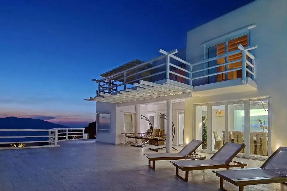 A modern villa opens onto a terrace with lounge seating and mountain views.