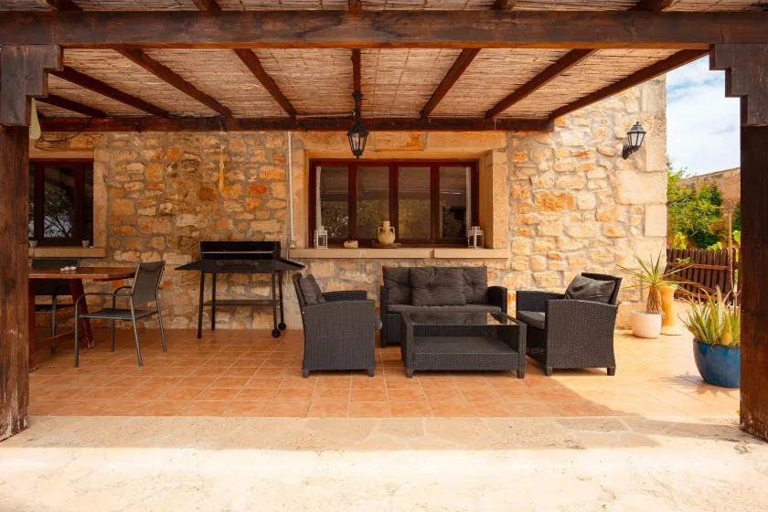 A covered outdoor patio has seating arranged beside a stone wall.