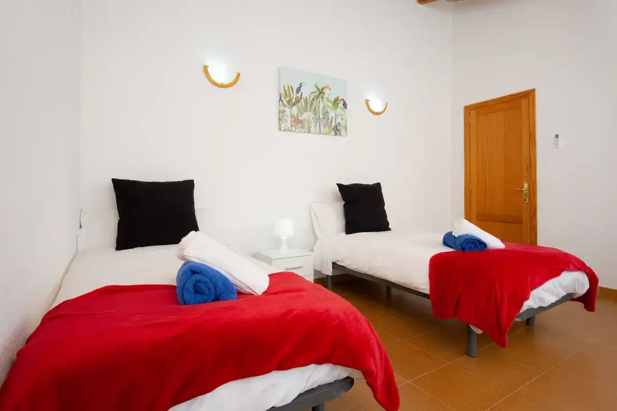 A bedroom with two beds dressed in white linens and red blankets.