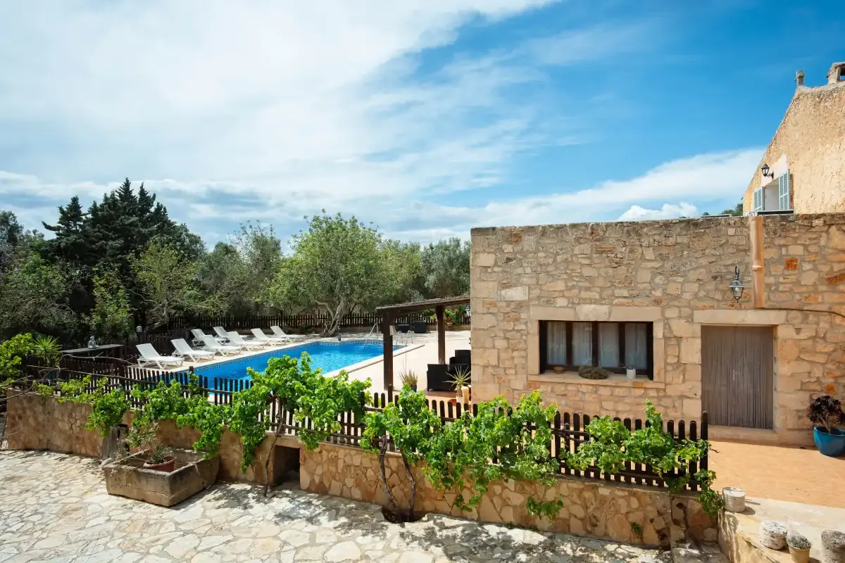 A stone house overlooks a swimming pool and a planted patio.
