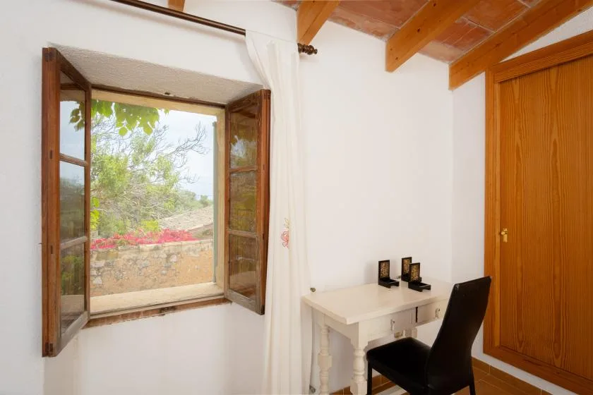 A small desk and chair sit beside an open window with wooden shutters.