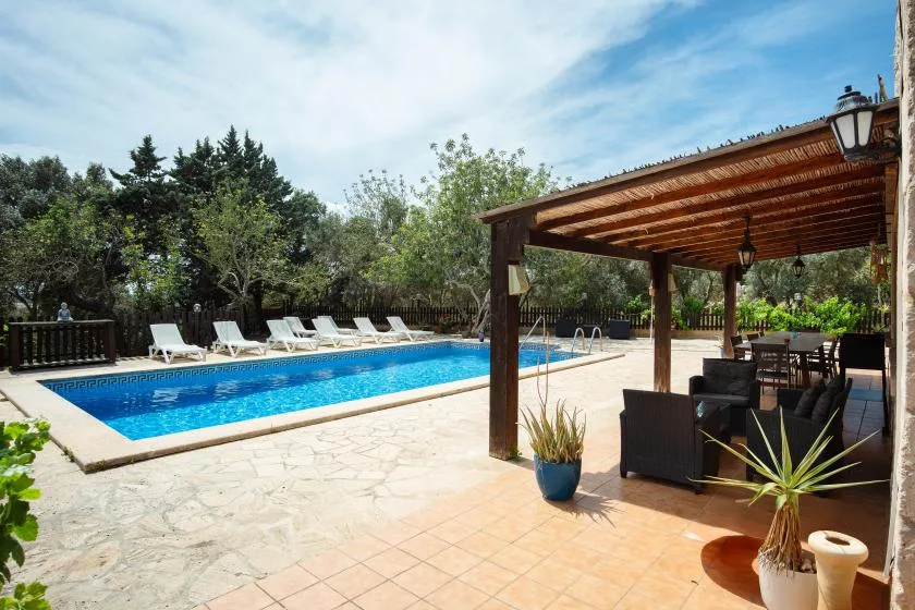 A swimming pool beside a shaded outdoor seating area and loungers.