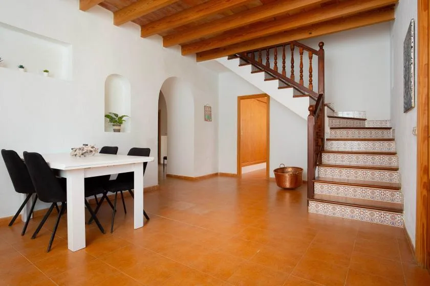 A bright dining area sits beside a tiled staircase beneath exposed wooden ceiling beams.
