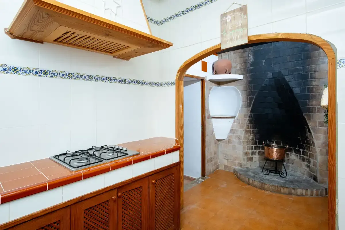 A tiled kitchen with a cooktop beside a large arched fireplace.