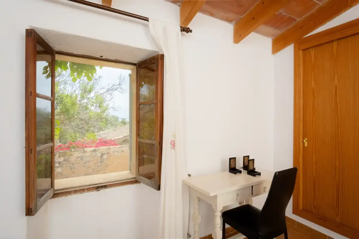 A small desk and chair sit beside an open window in a bright room.