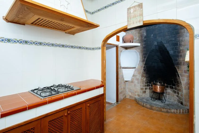 A tiled kitchen counter with a gas cooktop beside an arched brick fireplace.