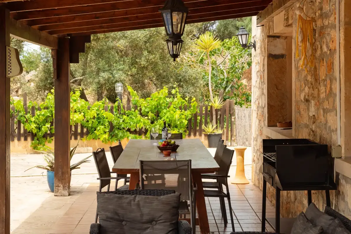 A covered outdoor dining area with a wooden table and garden beyond.