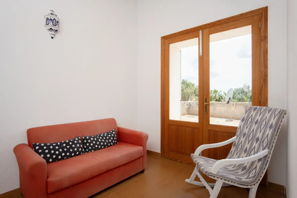 A bright living room with a red sofa and a patterned armchair beside the window.