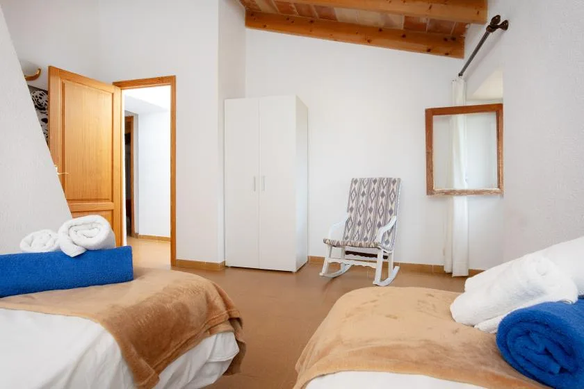 A bedroom with two beds, a wardrobe, and a rocking chair.