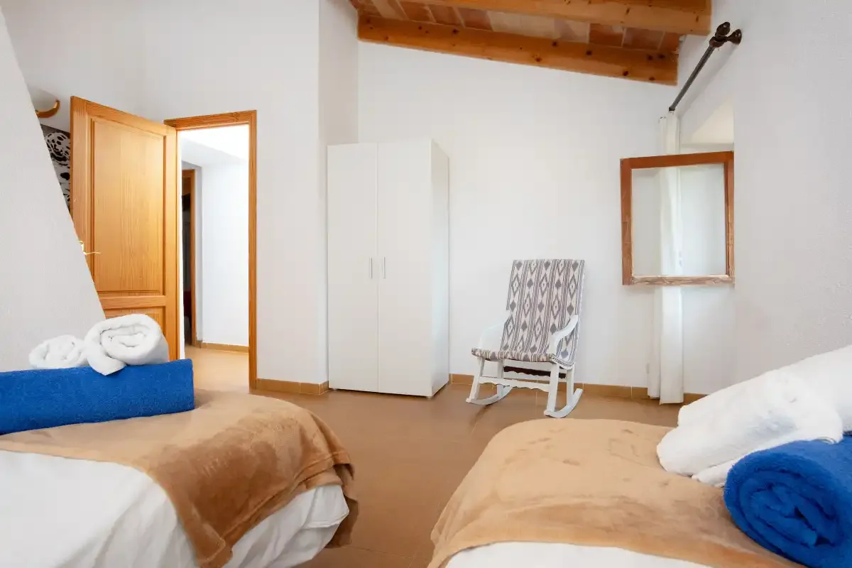 Bedroom with two beds, a rocking chair, and exposed wooden ceiling beams.
