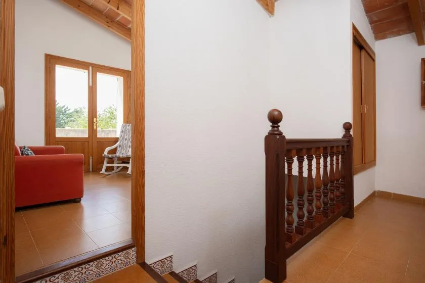 An interior hallway with a wooden stair railing and a bright adjoining sitting area.
