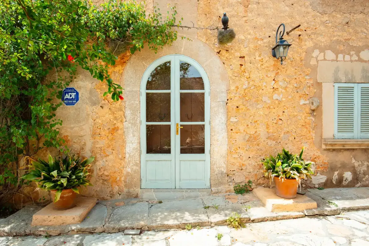 A pale blue arched doorway set into a stone exterior wall beside greenery.