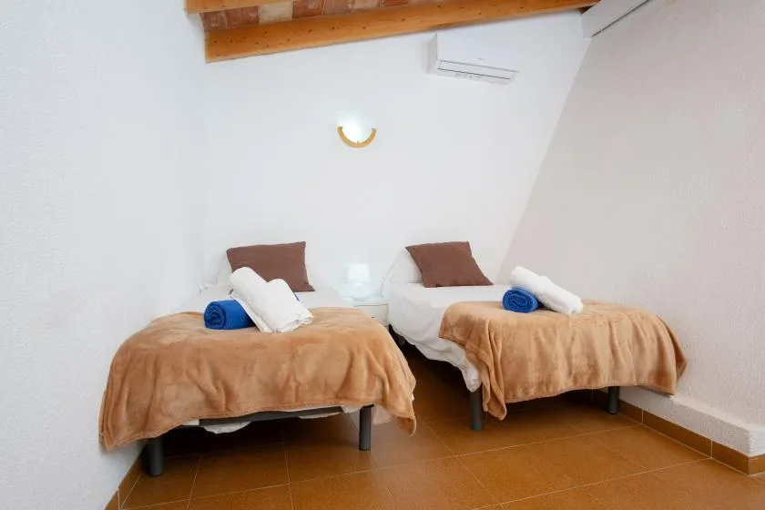 A bedroom with two separate beds, each dressed in a tan blanket.