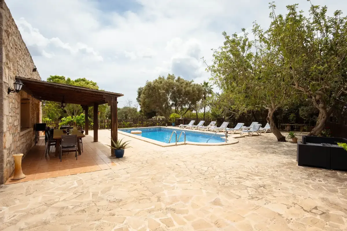 A stone-paved patio surrounds a swimming pool with loungers and shaded seating.