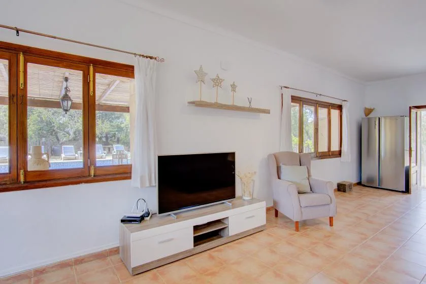 A bright living room with a television, seating, and large windows.