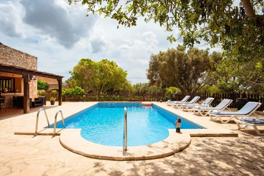 An outdoor swimming pool sits beside a shaded patio with lounge seating.