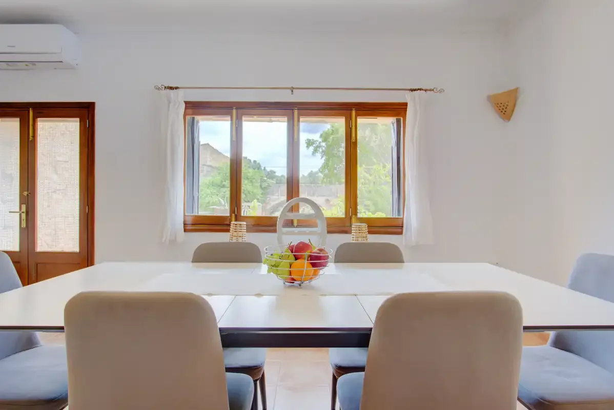 A dining area with a long table and a window overlooking greenery.