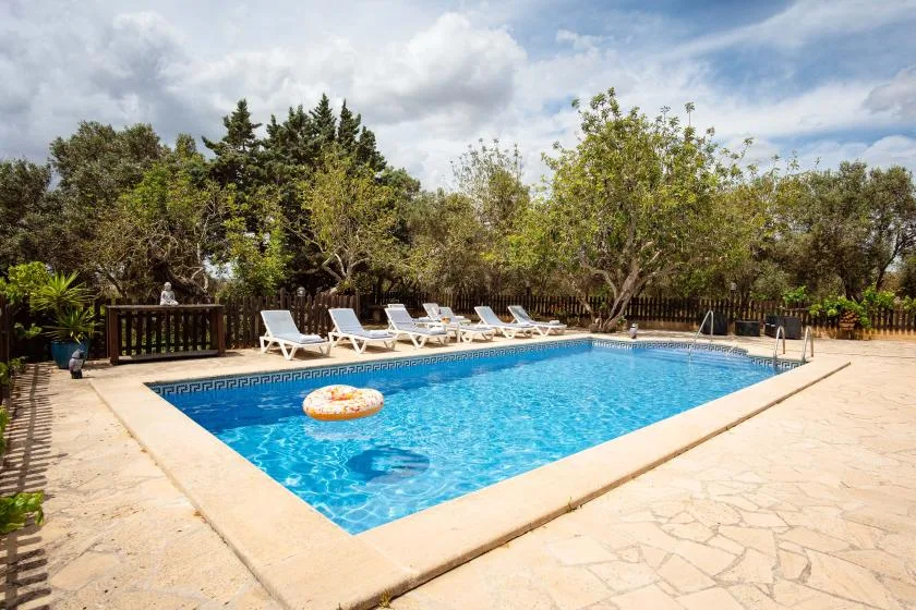 An outdoor swimming pool is surrounded by paving, loungers, and trees.