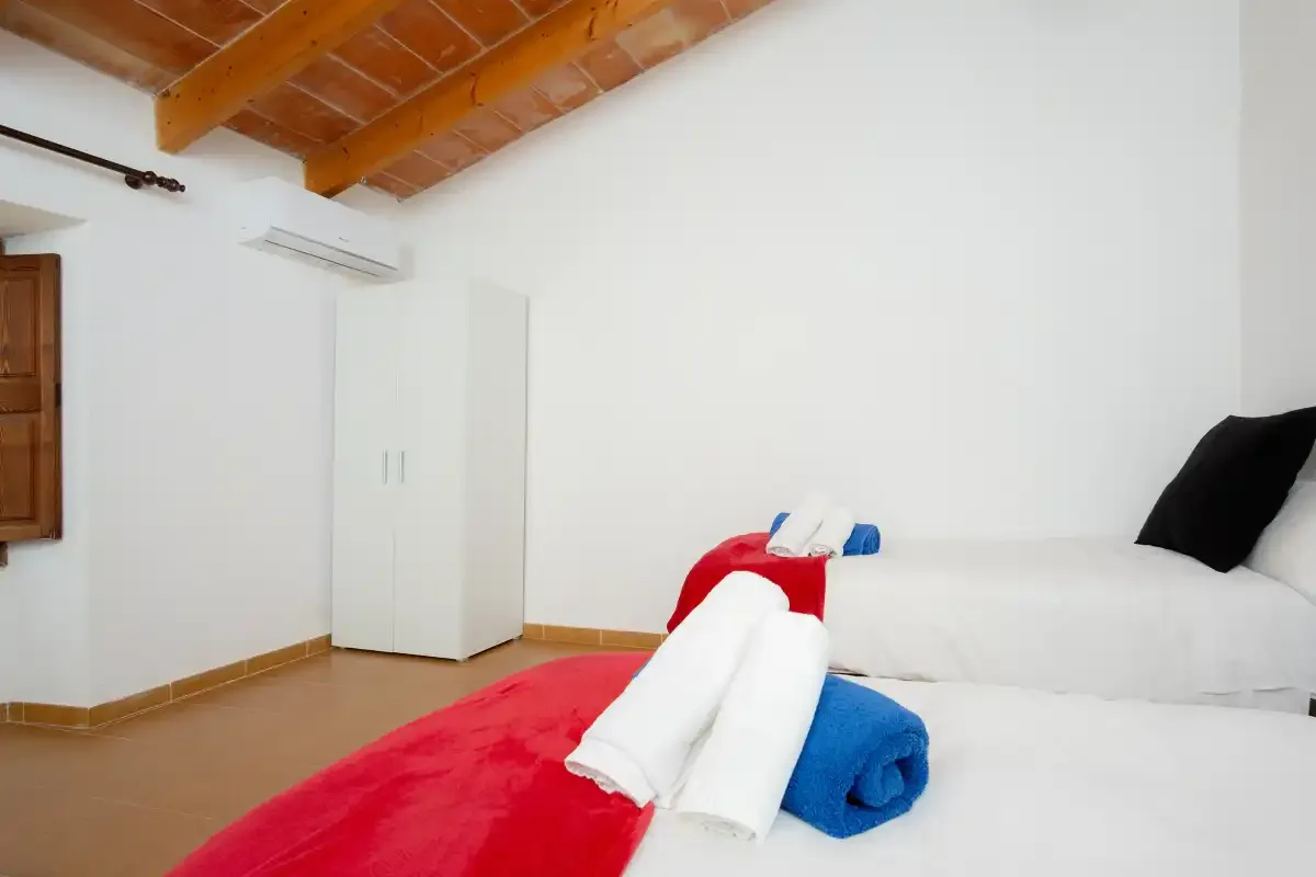 A bright bedroom with white beds beneath a wooden ceiling.