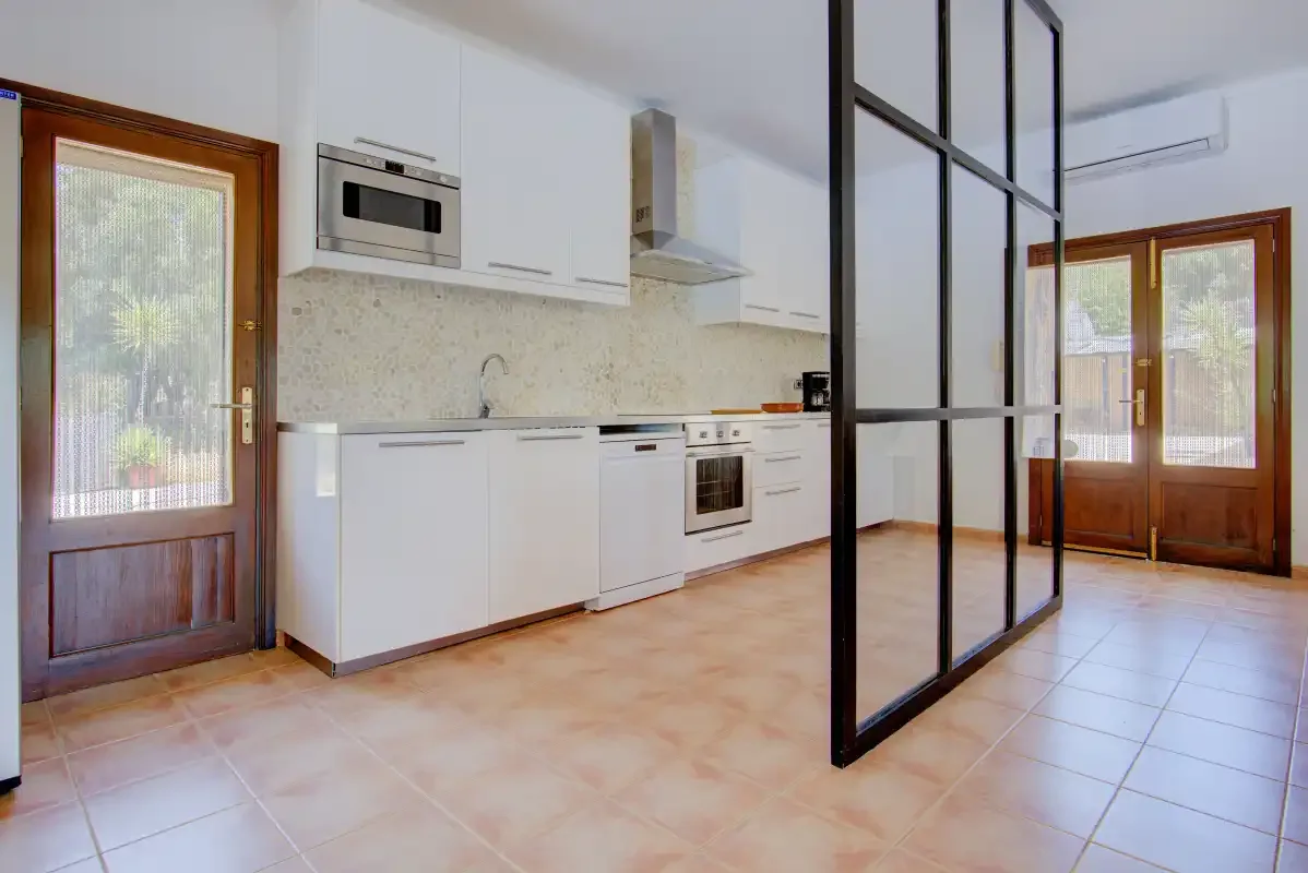 A bright kitchen with white cabinetry and glass doors opening onto the tiled interior.