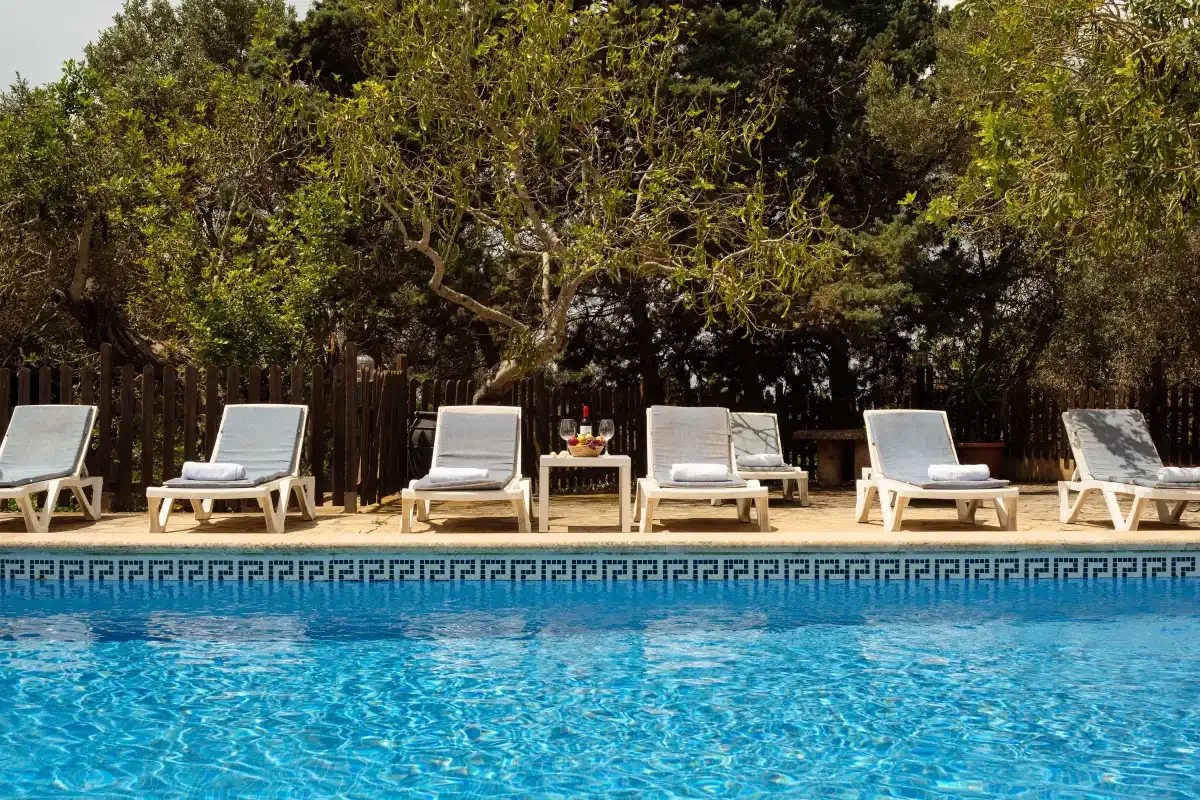 An outdoor swimming pool with lounge seating and trees behind it.