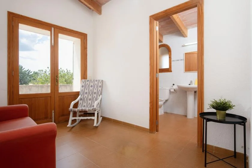 A bright room with wooden-framed windows, seating, and an open doorway to a bathroom.