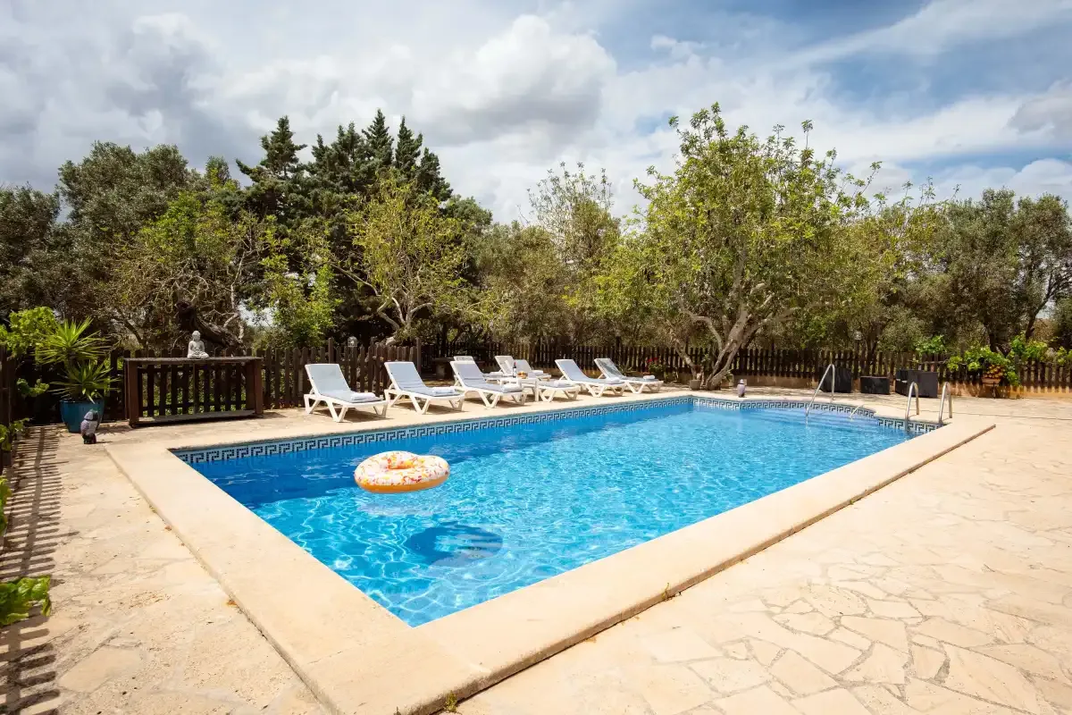 An outdoor swimming pool is surrounded by a paved patio and trees.