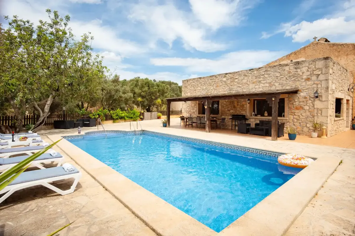 A swimming pool beside a stone building, with loungers along the pool deck.