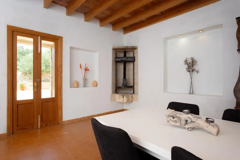 A dining area with a white table and dark seating beneath exposed wooden ceiling beams.