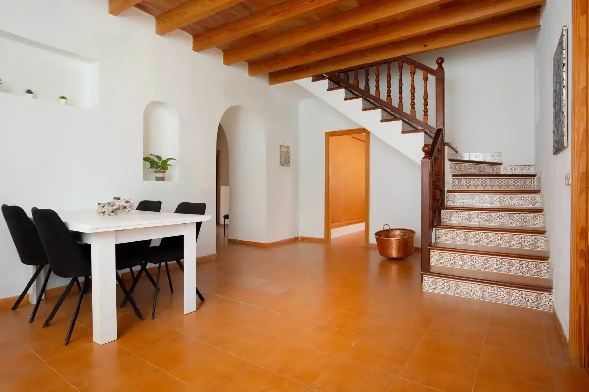 A dining area and tiled staircase share a bright interior with exposed wooden beams.