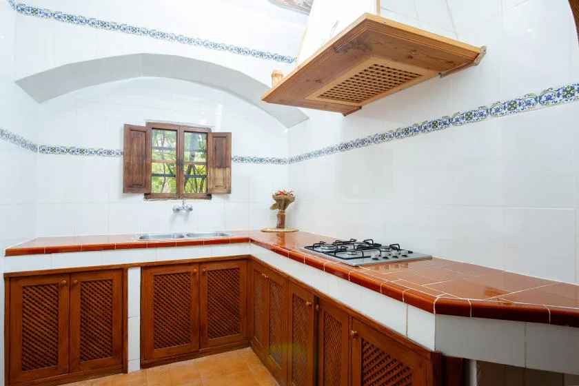 A tiled kitchen with wooden cabinets, a cooktop, and a small window.