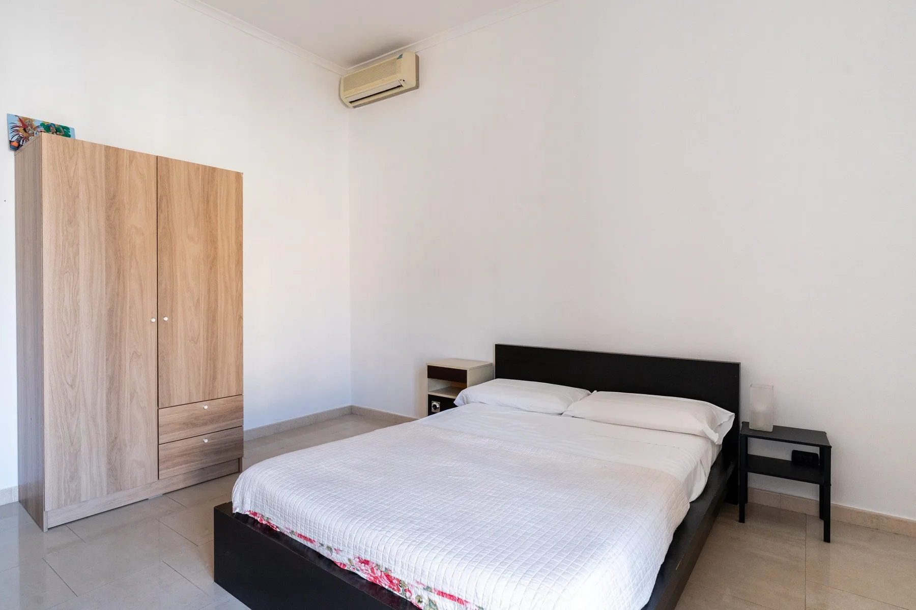 Un dormitorio con una cama, un armario de madera y un aire acondicionado.