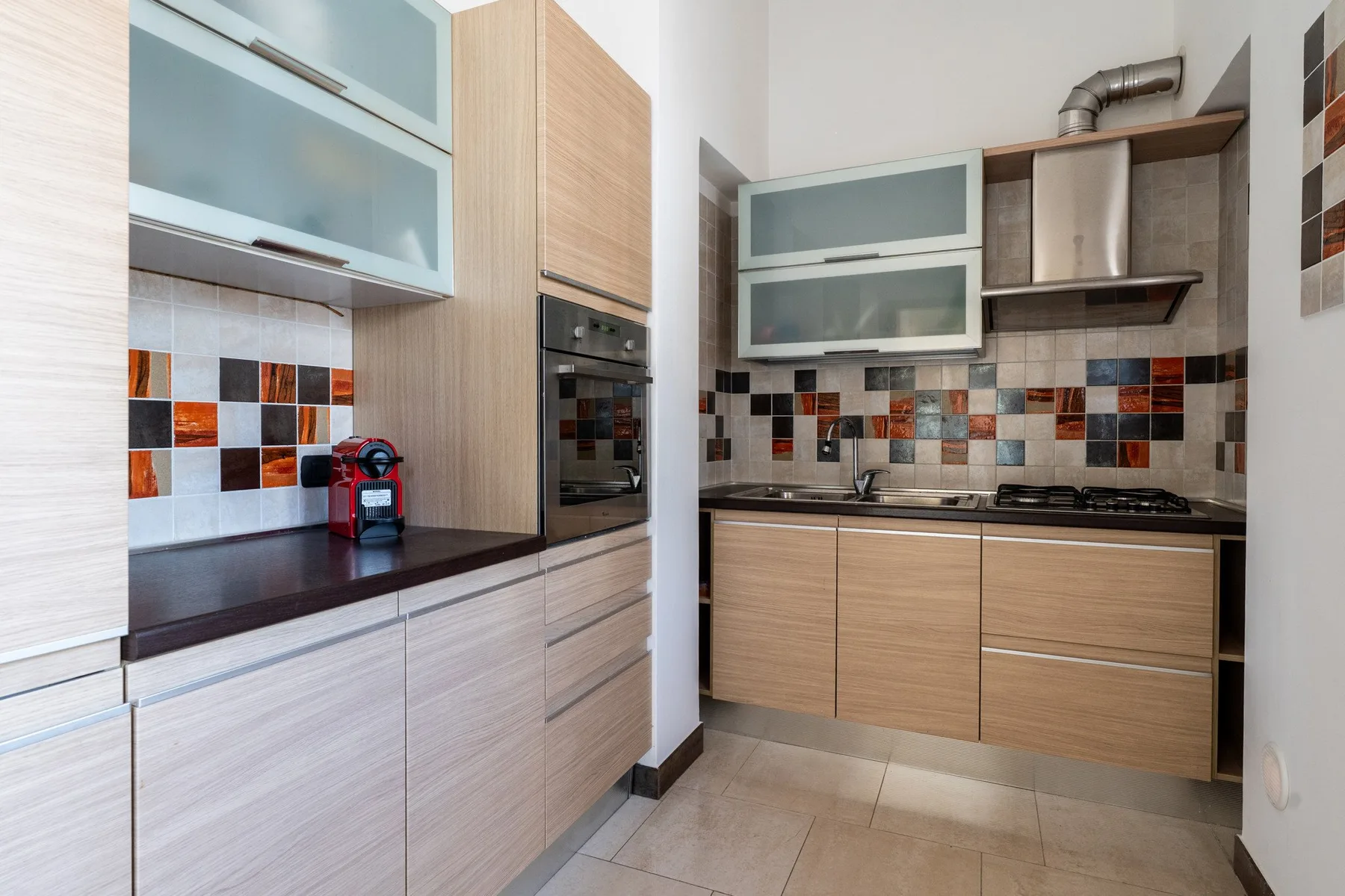 Una cocina moderna con gabinetes de madera clara, una estufa y un salpicadero de azulejos coloridos.