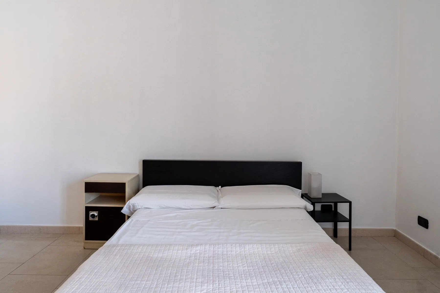 Un dormitorio con cama doble, mesitas de noche y paredes blancas lisas.