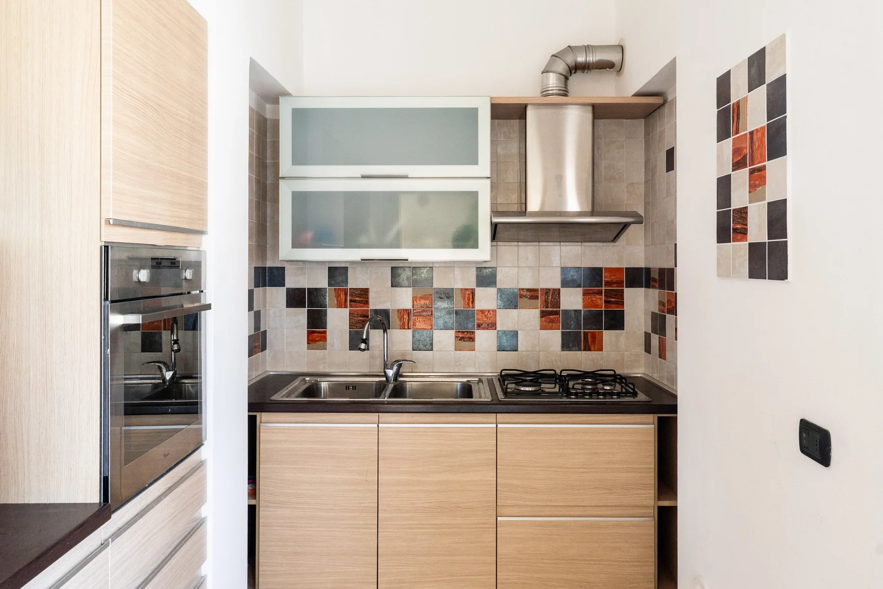 Una cocina moderna con gabinetes de madera clara, un salpicadero de azulejos y un horno empotrado.