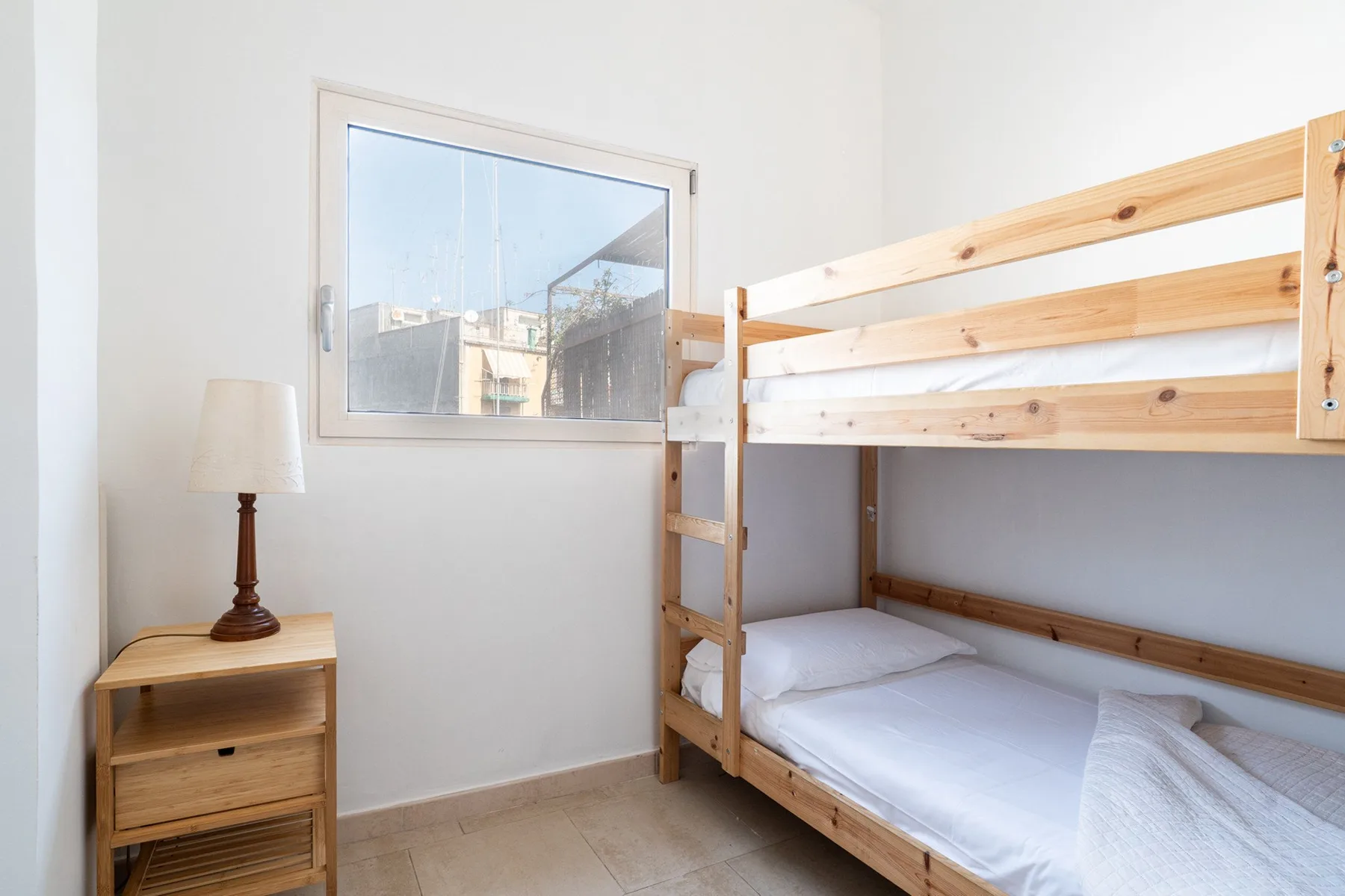 Un dormitorio con una litera de madera, una mesita y una ventana.