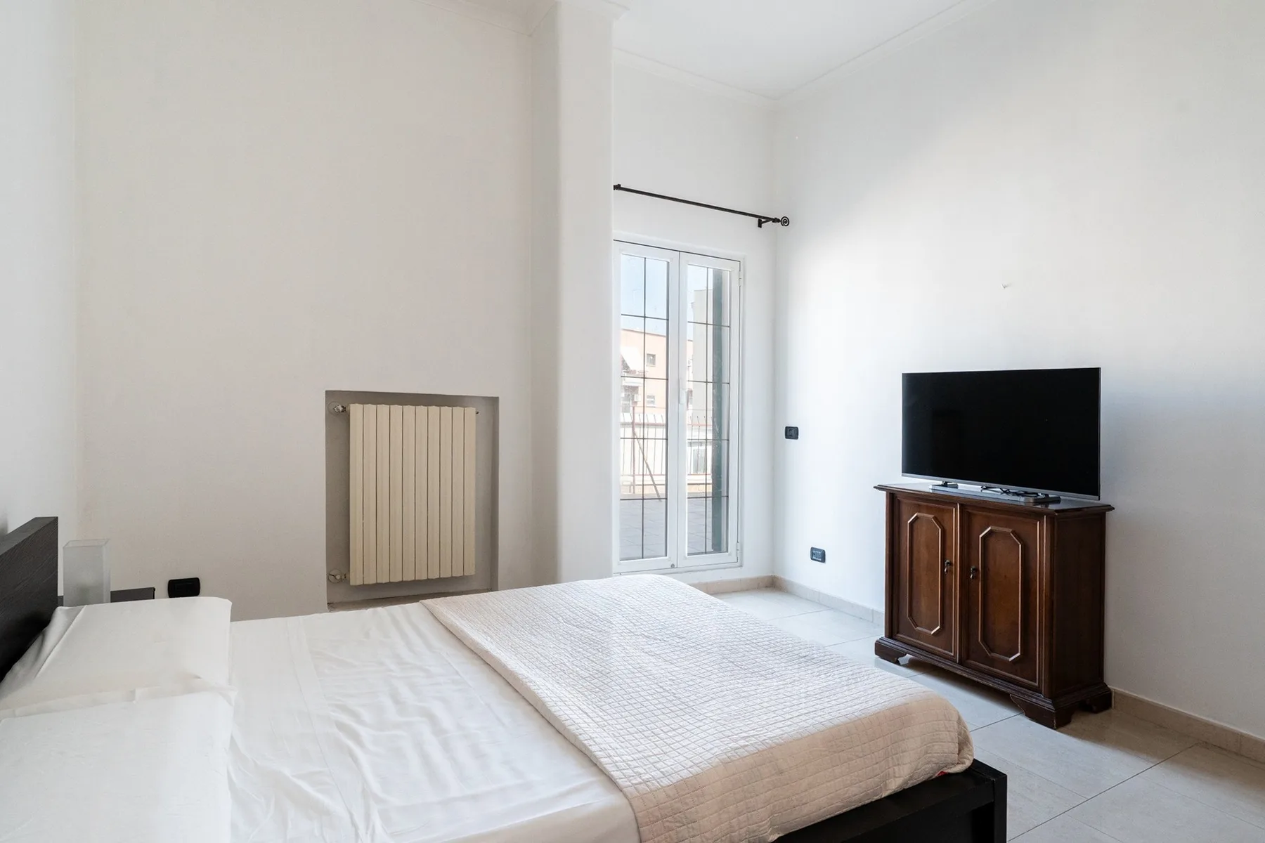 Un dormitorio luminoso con una cama, una puerta de vidrio y un televisor sobre un mueble.