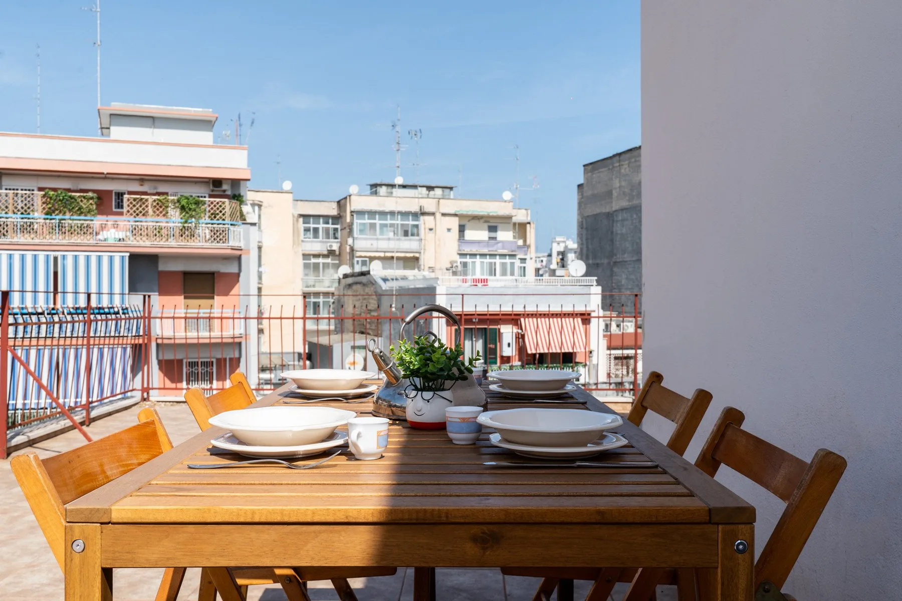 Una mesa de comedor al aire libre con platos puestos da a edificios y balcones vecinos.