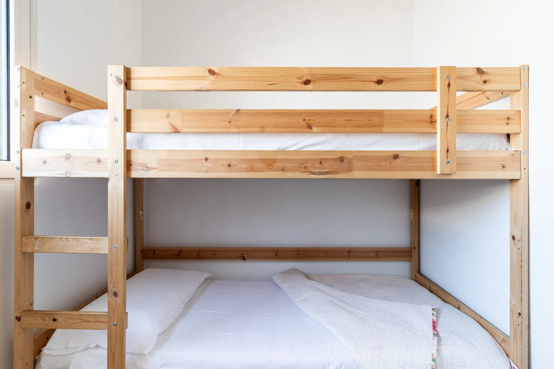 Una litera de madera con ropa de cama blanca en un dormitorio luminoso.