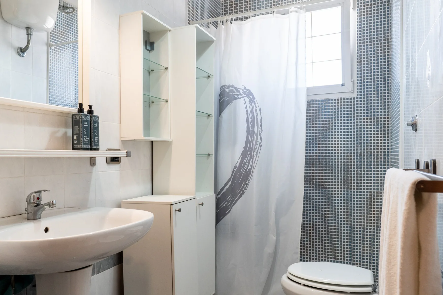 Un baño con lavabo, inodoro y cortina de ducha junto a paredes alicatadas.