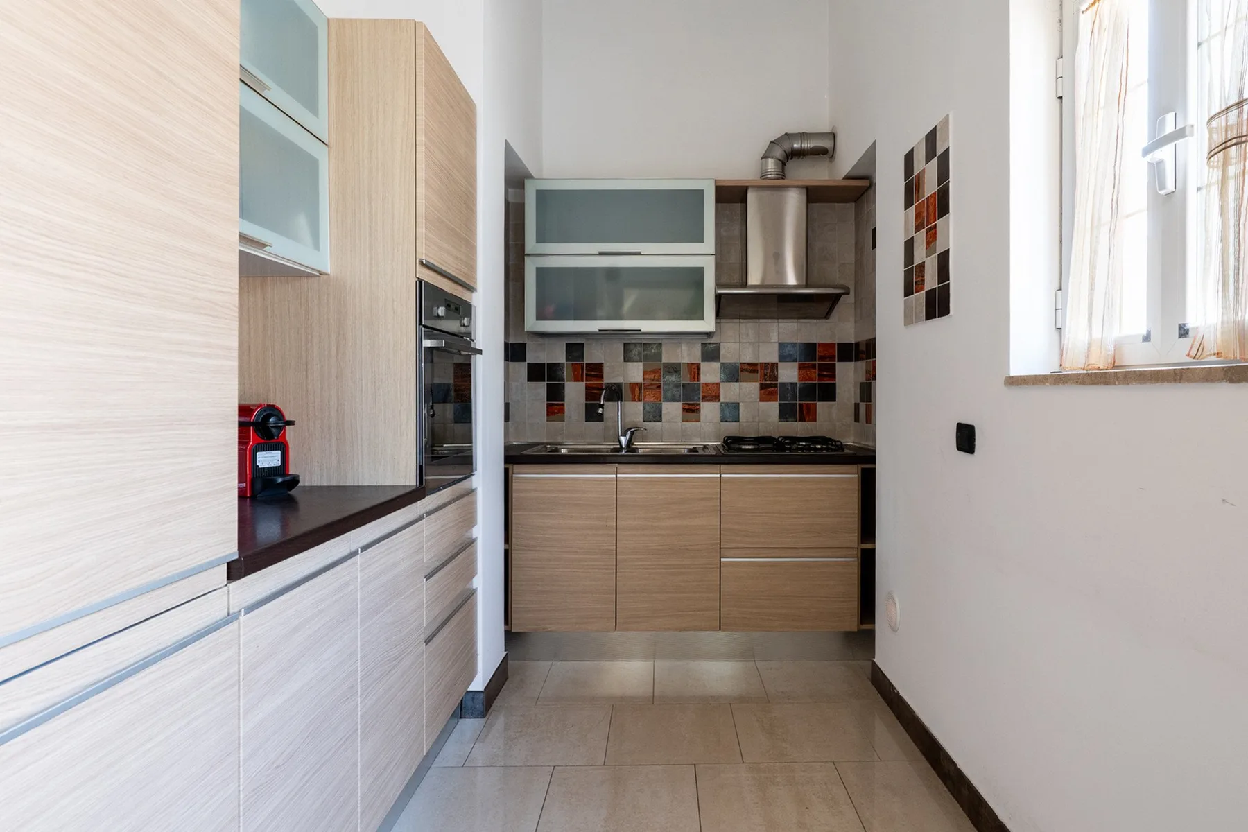 Una cocina moderna con gabinetes de madera clara y un salpicadero de azulejos coloridos.
