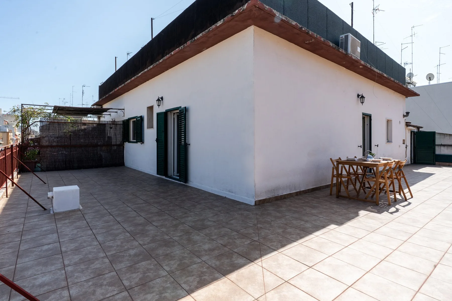 Una terraza pavimentada rodea un edificio blanco, con asientos y una mesa al aire libre.