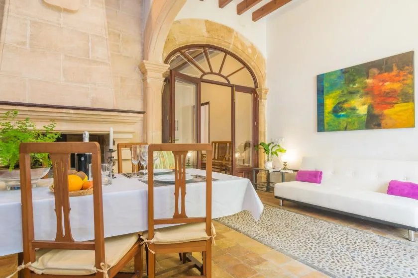 A dining area with wooden seating, a long table, and colorful artwork on the wall.