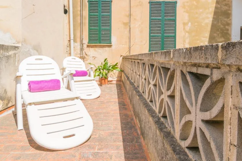 A sunlit terrace with white lounge seating beside a decorative railing.