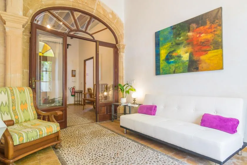 A bright sitting room with a white sofa, colorful cushions, and an arched glass doorway.