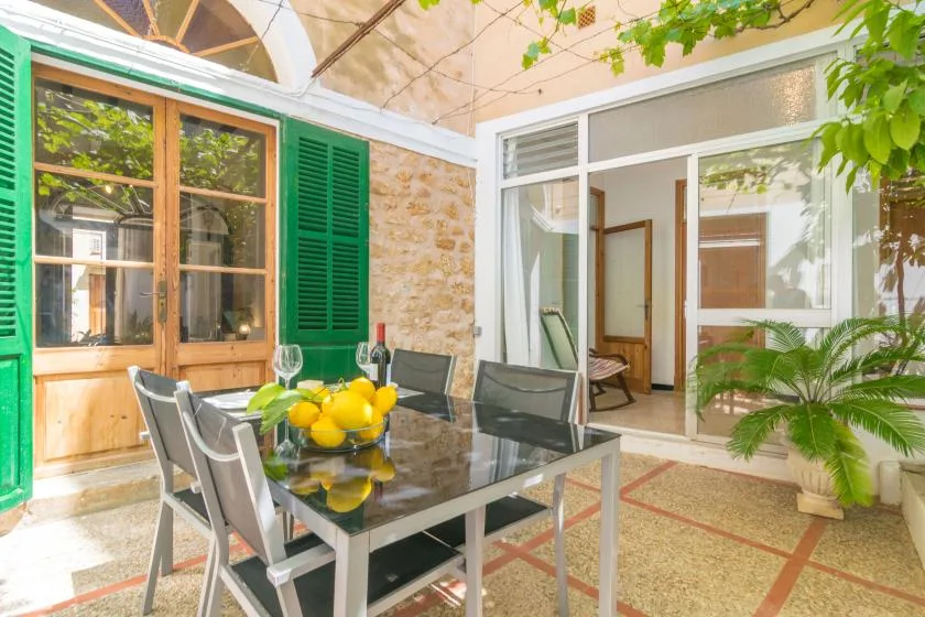 A bright patio dining area with a glass table and green shutters.