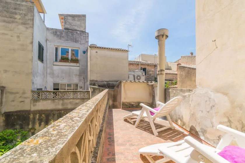 A sunlit rooftop terrace with reclining seating and surrounding buildings.