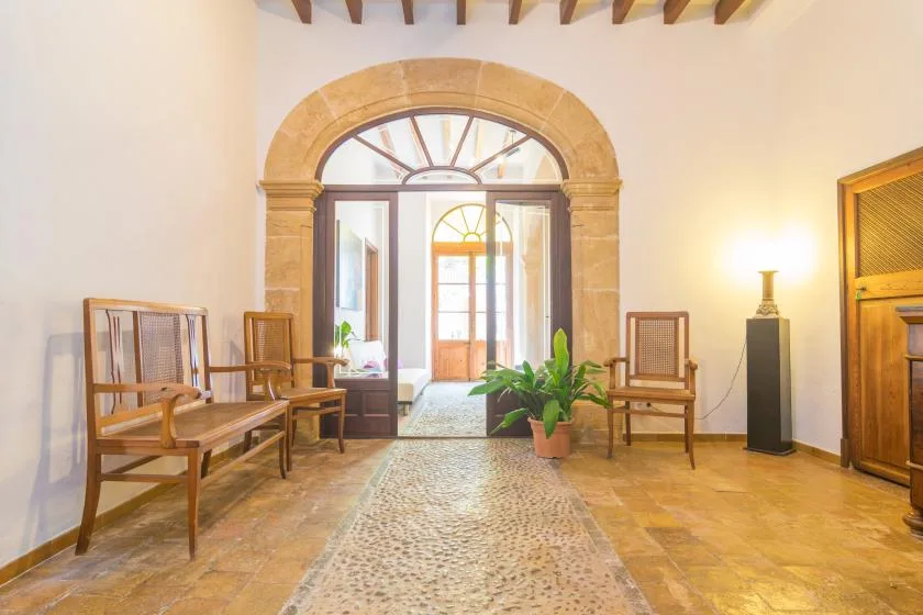 A bright interior hall with a stone archway, wooden seating, and potted plants.