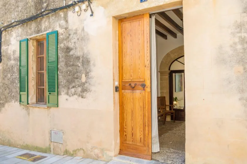 An open wooden doorway and a window with green shutters on a weathered exterior wall.