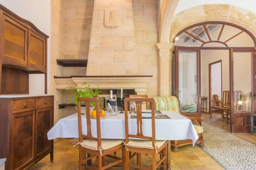 A dining room with a table set beside a large stone fireplace.